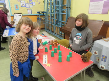 A stall at a school fair with green cups on the table, with three children standing by the table and smiling