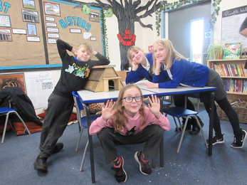 Four schoolchildren gather round a table in a classroom, showing off their wooden hedgehog house