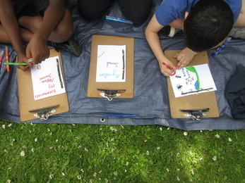 Three children pictured from above as they sit on the ground and create paper nature journals