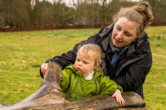 A woman and child play outside on a rainy day, looking at a tree branch together