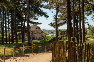 Holme visitor centre between the trees with a wooden picket fence and sandy path. 