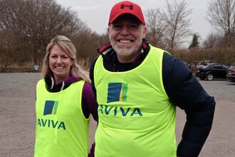 Two people wearing fluorescent yellow vests with the Aviva logo on the front smile at the camera