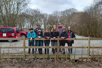 A group of young people stand behind a fence smiling on a cloudy day
