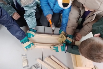 A group of children pictured from above using hammers to build a nest box