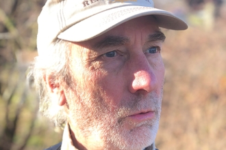 A man with grey stubble and wearing a cap looks off to the right