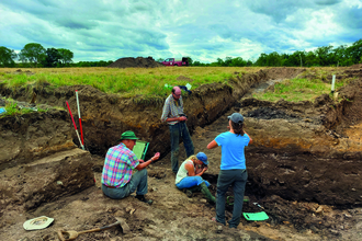 Four people gather around a post pingo excavation site chatting and studying rocks and dirt. 