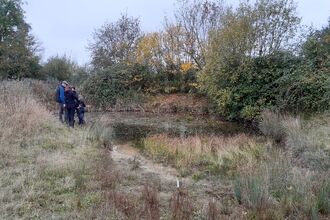 Three people gathering around a pond during the winter. 