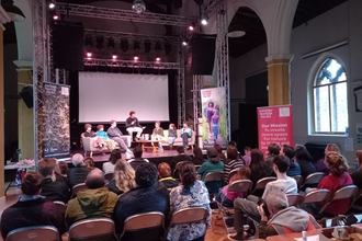 A photo from our Youth Action Now event - there is a panel of six young people on stage and a few rows of people in the audience. 