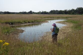 A woman in a bucket hat standing on the edge of a flooded pingo pond