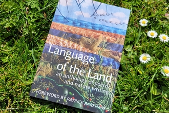 A book called Language of the Land sits on a patch of grass and daisies