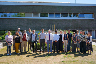 A group photo of UEA and NWT staff as they join together to sign a memorandum of understanding. It's a sunny day and they are posing in front of a university building.