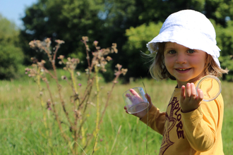 A child holds a bug pots and smiles in a meadow