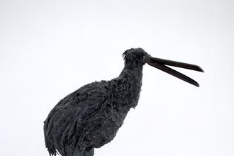 A rough brown metal sculpture of a kiwi standing on a square wooden plinthen 