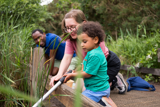 A child pond-dips with the help of their parents