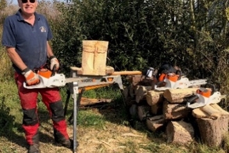 Chainsaw artist volunteer, Andy Usher, grinning with his tools and creations outside at Hickling.