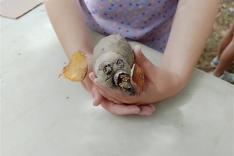 An image of a small girl's hands holding a clay animal with acorn eyes and nose