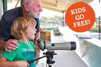A child looks through a telescope with his grandfather at Cley visitor centre
