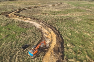 An aerial photograph of winding restoration works being carried out by an orange and blue digger in the foreground