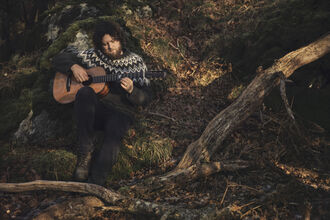 a man playing guitar sitting on some tree roots