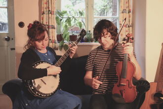 Christina is playing a banjo and Alex is holding a fiddle and bow