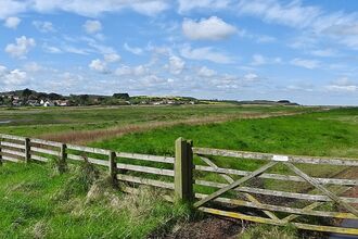 The view across Cley Marshes towards Cley village, standing in front of a five-barred gate