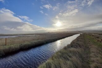 a dyke running through marshes, with a big sky
