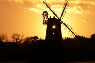 Cley windmill and trees silhouetted against a golden sunset