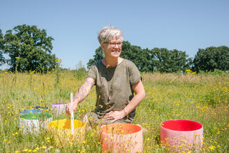 A lady sitting in a summer meadow with 4 brightly-coloured round crystal bowls