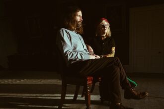 Musicians Samantha Whates and MG Boulter are seated facing sideways -on, in a dark room