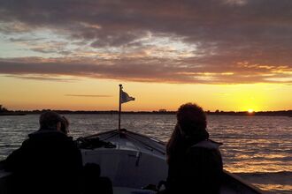 Two people sail a boat across Hickling Broad as the sun comes up