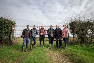 A group of people in wellies smiling and posing together in front of a farm gate. 