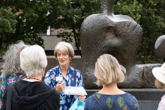 A group of people with a walk leader standing in front of a large sculpture