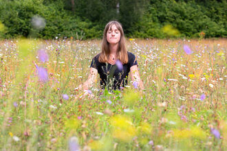 A woman seated in a yoga position in a wildflower meadow