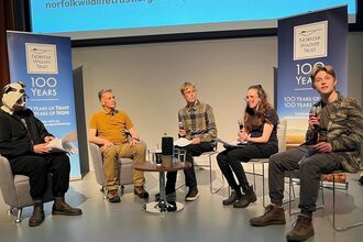 A line of people on stage conducting an interview. The person on the far left is dressed as a badger, while the young adult on the far right speaks into a microphone