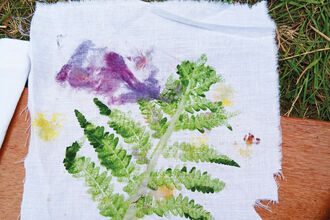 A piece of white material with a green fern leaf and purple flower print on it
