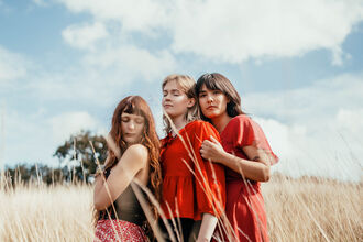 Murmurations band members wearing brightly coloured clothing and standing in a meadow of yellow grass