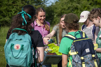 A group of young people outdoors smiling and taking gardening gloves from a box.