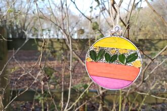 A pink, yellow and green Christmas bauble made out of paper and foraged leaves