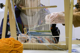 Two ladies creating a colourful woven tapestry on a wooden loom