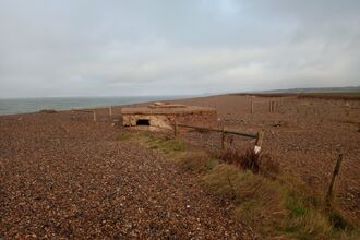 A WW2 military building on a shingle beach, with the sea in the distance