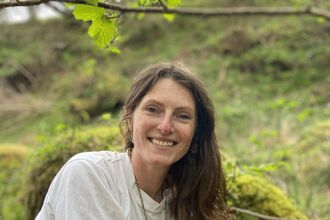 Lucy is wearing a white t shirt and is sitting in woodland, smiling at the camera 