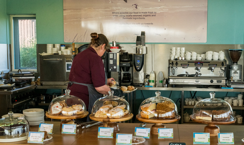 Member of staff working in a cafe, with stands of cakes in the foreground
