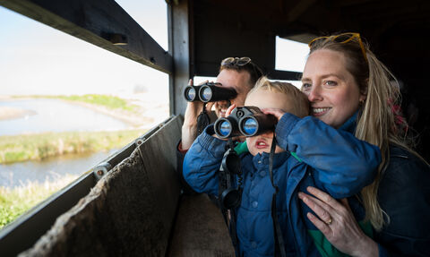 A young family peering out a wildlife hide with binoculars at Cley.