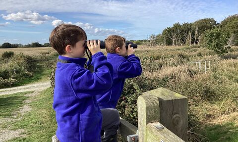Two primary school children in uniform looking through binoculars at a nature reserve