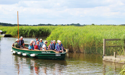 A small boat full of smiling people in life jackets on Hickling Broad on a sunny day 