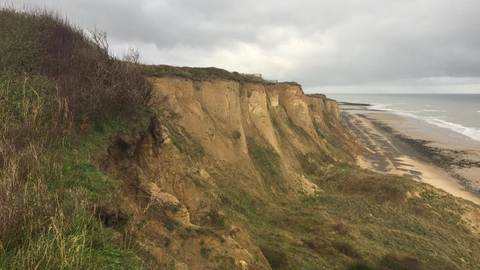 Sandy, grassy cliffs sweep down to a beach on a grey day