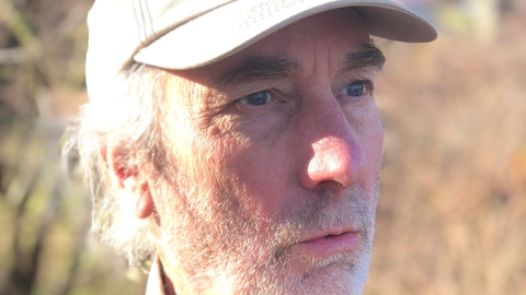A man with grey stubble and wearing a cap looks off to the right