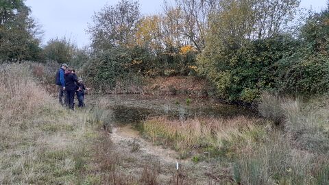 Three people gathering around a pond during the winter. 