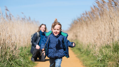 A young boy happily runs towards the camera brandishing a stalk of reed