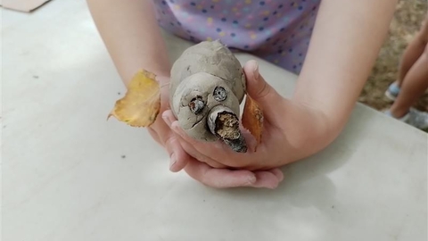 An image of a small girl's hands holding a clay animal with acorn eyes and nose